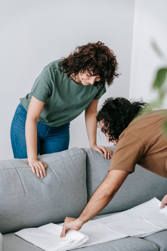 A couple getting the living room ready by covering the couch with a protective white cloth.
